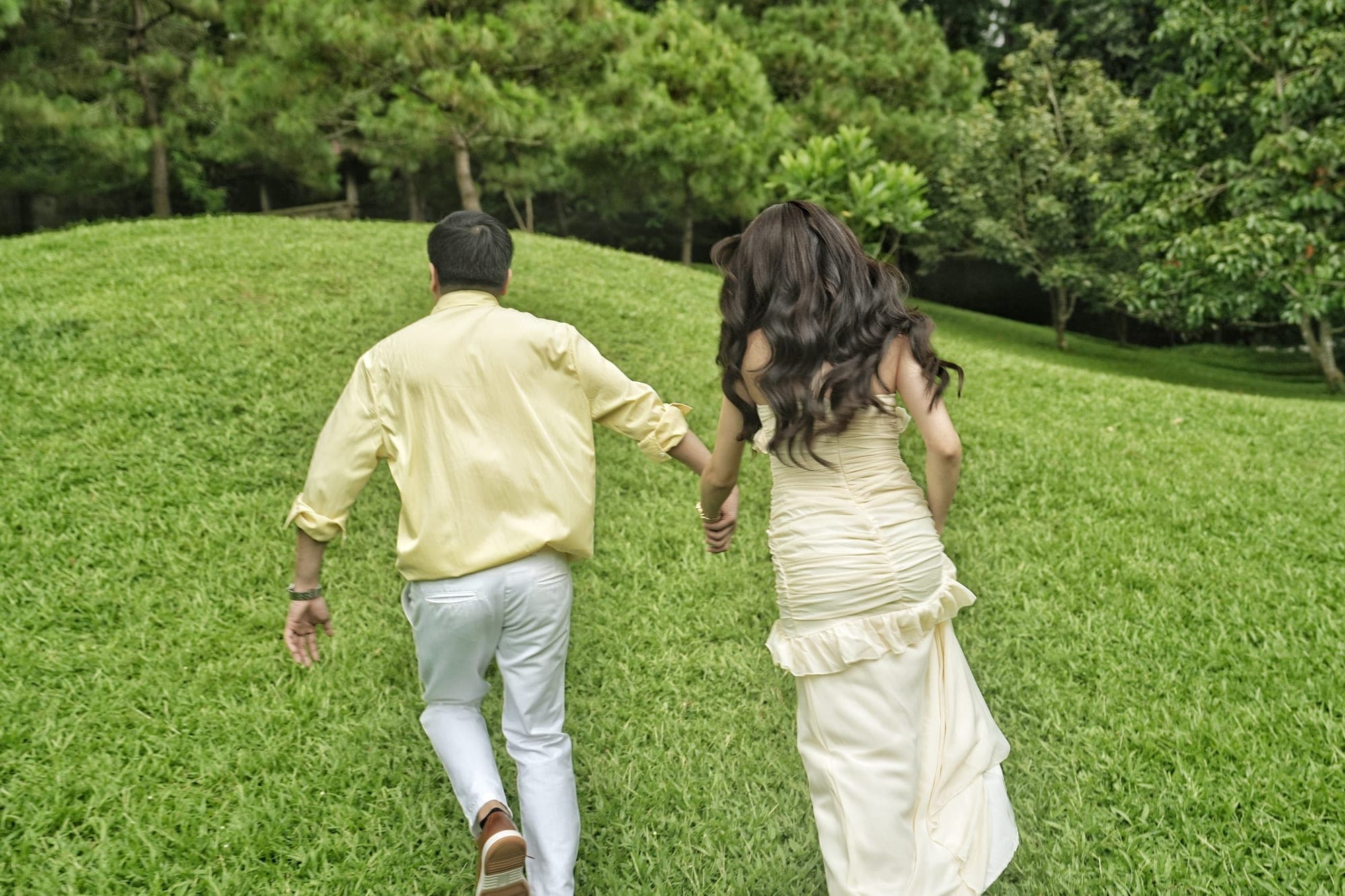 Justin and Lovely, in matching pale yellow outfits, walking hand in hand away from the camera up a grassy hill