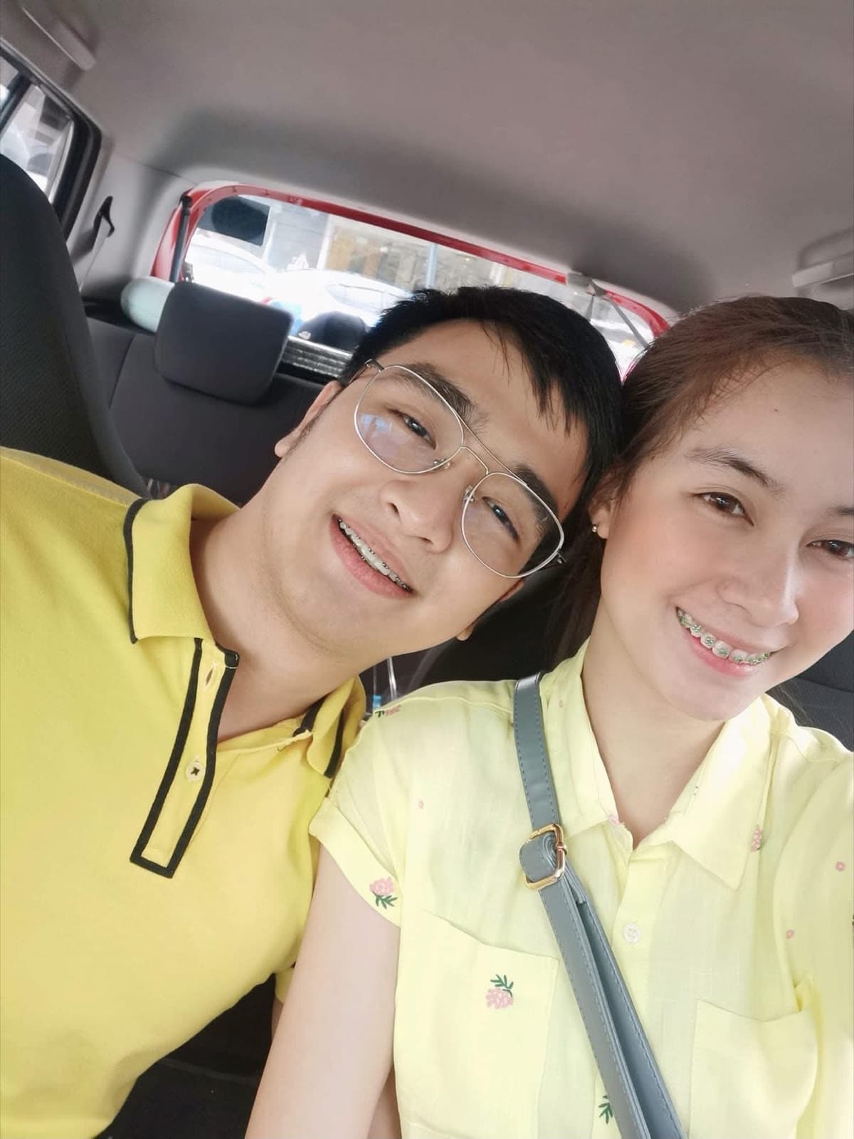 Justin and Lovely in matching yellow tops, smiling close together in a car selfie